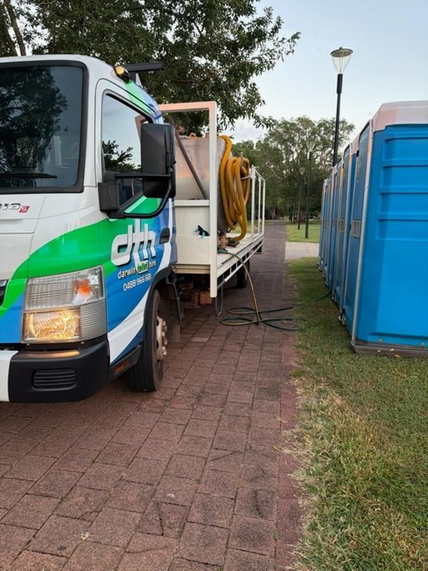 White-and-green Utility Truck Beside a Blue Dumpster on a Brick Path in a Park-like Area — Darwin Toilet Hire in Palmerston, NT