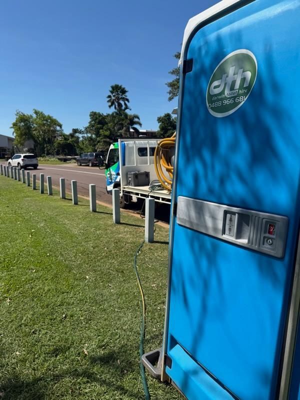 Blue Portable Toilet Beside a Grassy Roadside With Parked Utility Vehicles — Darwin Toilet Hire in Katherine, NT