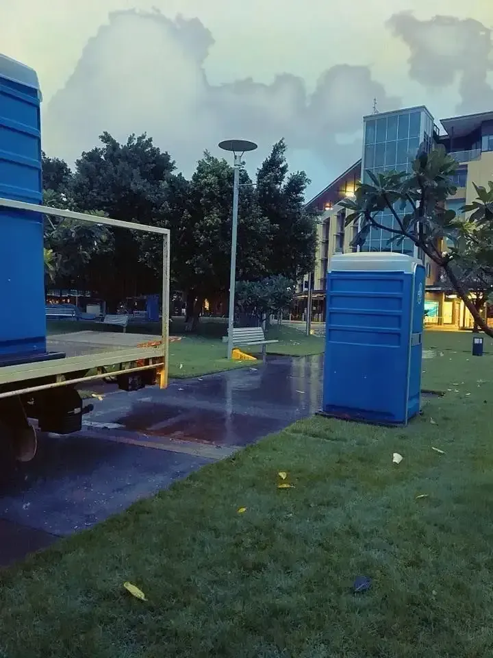 Rainy Park With Blue Portable Toilets, a Truck, and Trees in the Background — Darwin Toilet Hire in Rosebery, NT