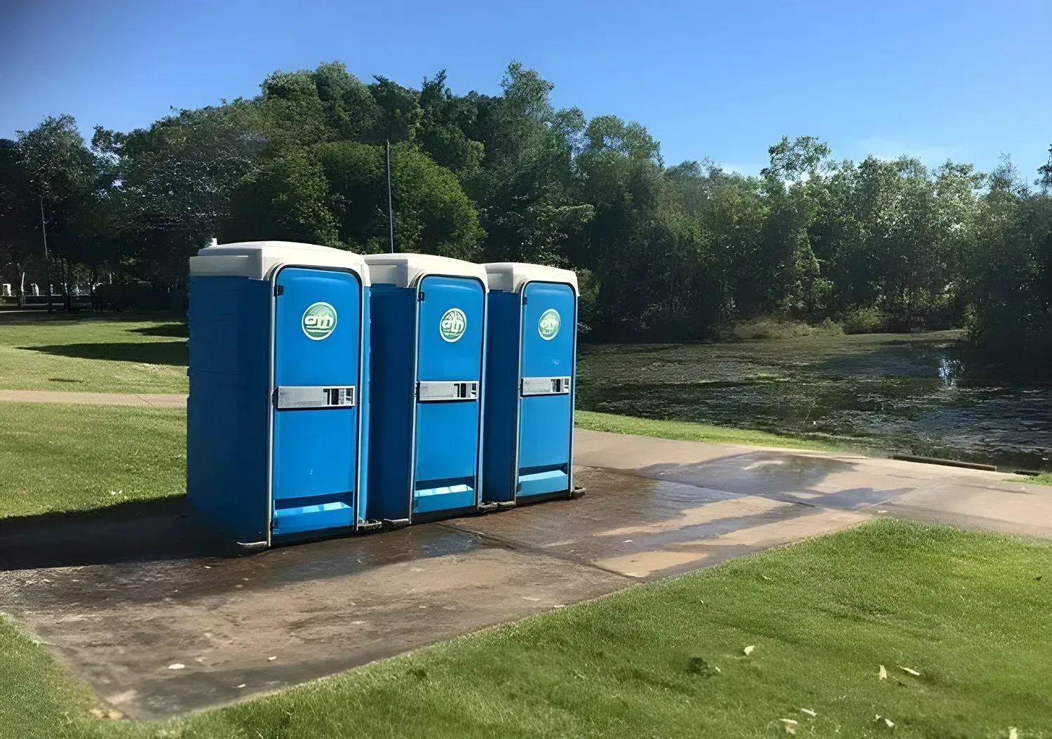 Three Blue Portable Toilets Beside a Paved Path in a Grassy Park Area — Darwin Toilet Hire in Rosebery, NT