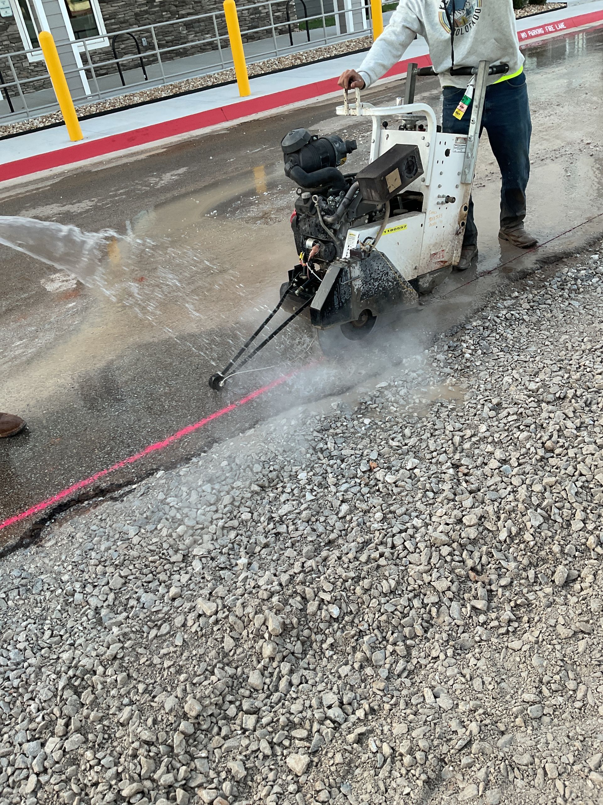Person operating a pavement saw cutting along a red line; water is spraying.