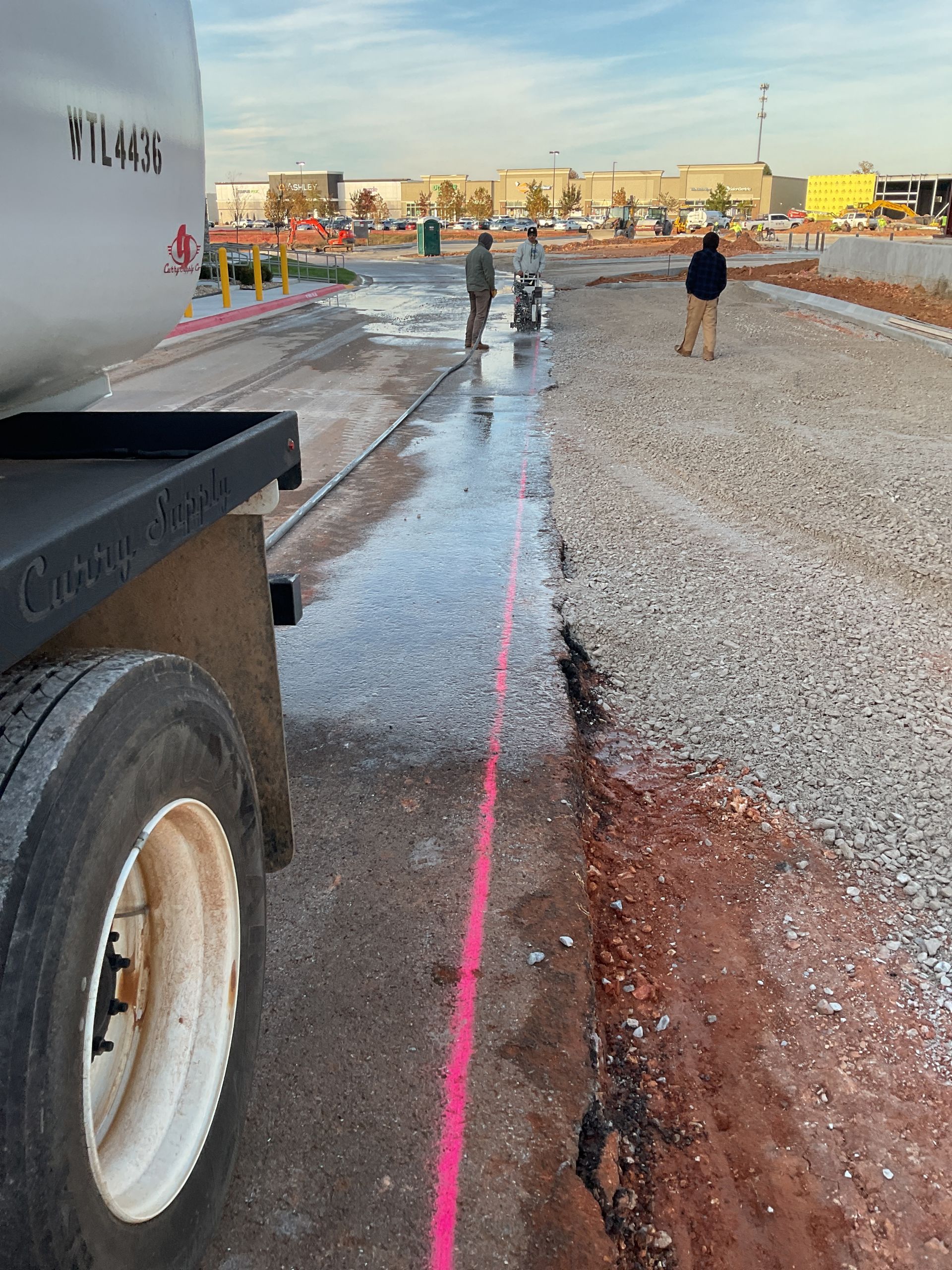 Construction site with a truck, worker using saw, pink line, and gravel.