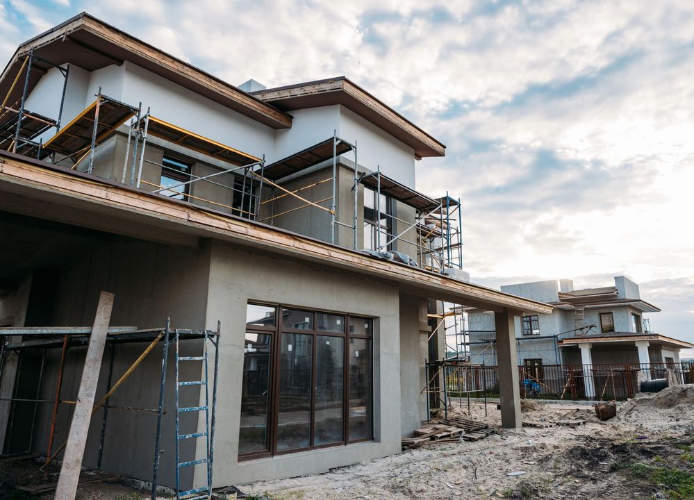 Casa in costruzione con impalcature, cielo nuvoloso sullo sfondo.