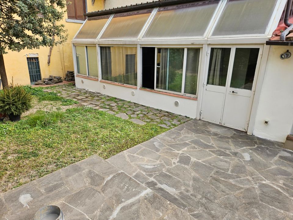 Mano di una persona che tiene le chiavi con un portachiavi a forma di casa, di fronte a una scrivania sfocata.