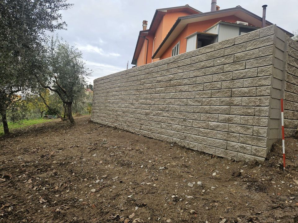 Mani di un muratore che posizionano un mattone su un muro parzialmente costruito con la malta.
