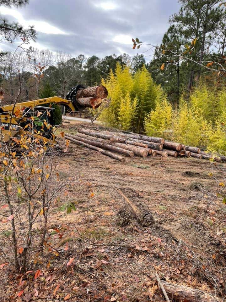 A pile of logs in a field with a bulldozer in the background.