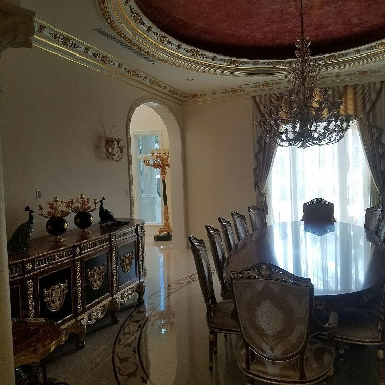 Ornate dining room with a large table, chandelier, and decorative sideboard. Gold accents, red ceiling.