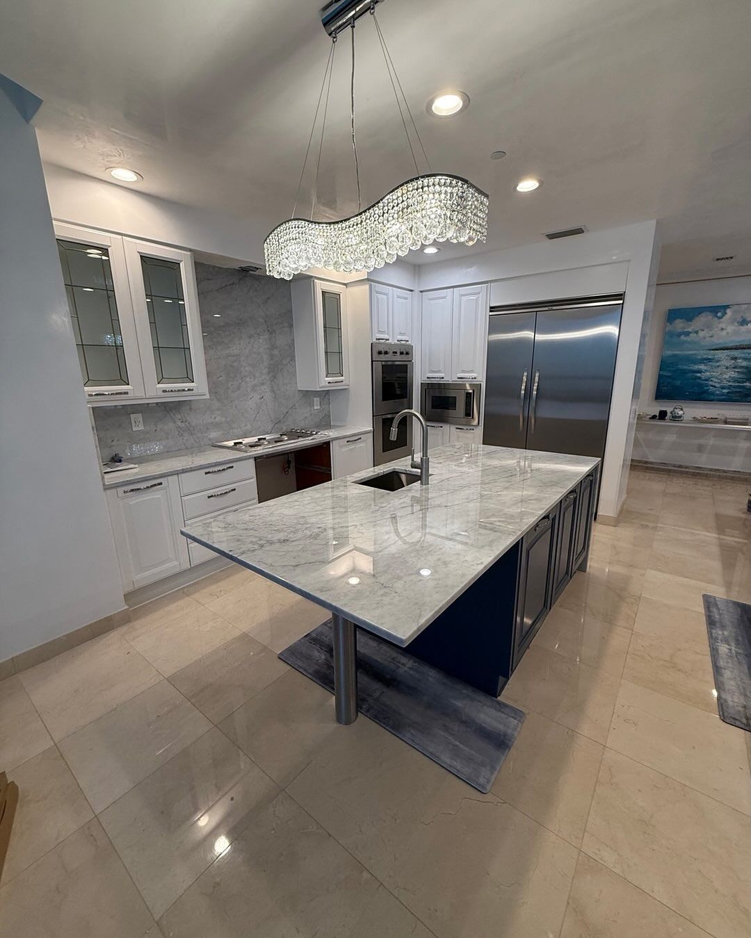 Modern kitchen with a large island, stainless steel appliances, and a crystal chandelier.