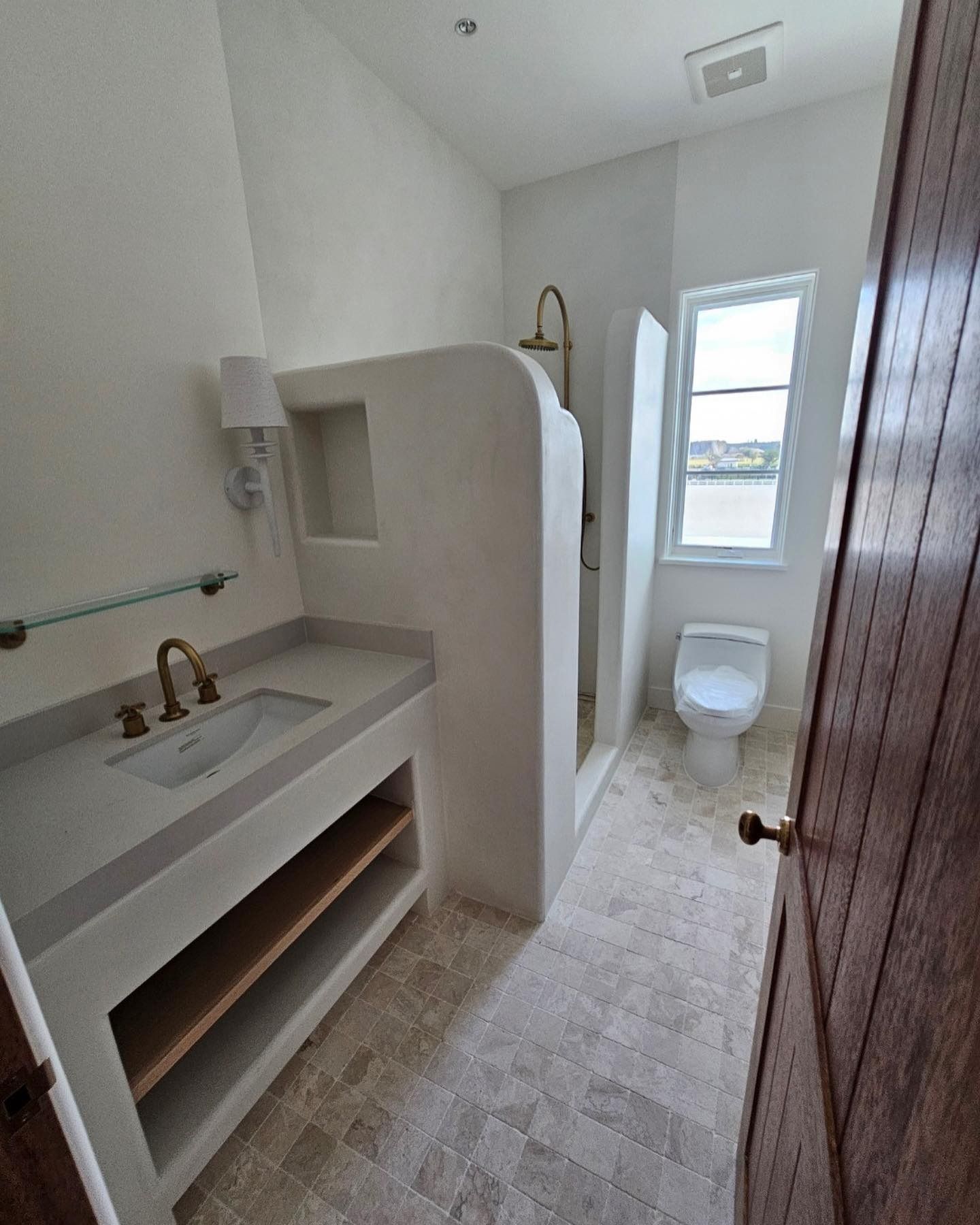 Bathroom with white walls, sink, shower, toilet, and wooden door.