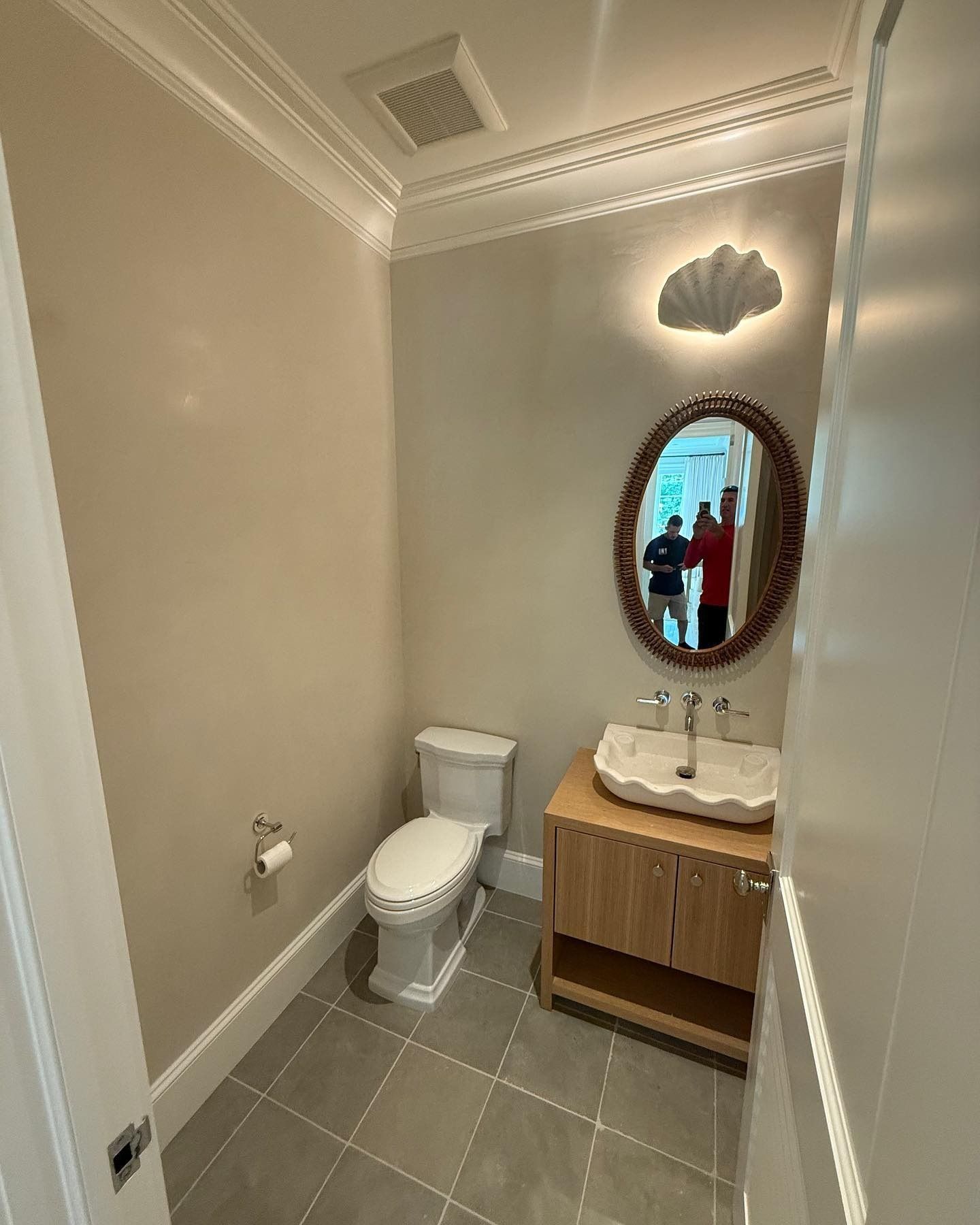 Small bathroom with toilet, sink, oval mirror, and light fixture on a neutral-colored wall.