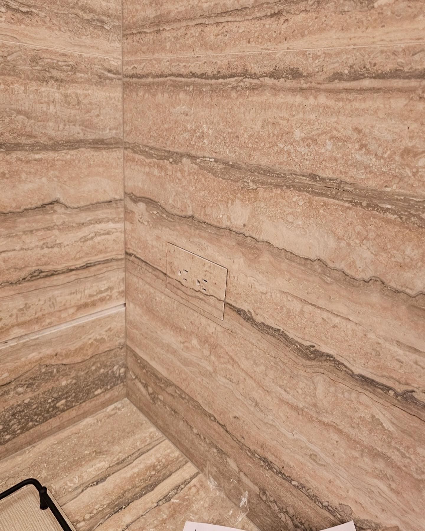 Corner of a bathroom shower with tan, layered stone tile. There is a rectangular access panel in one wall.