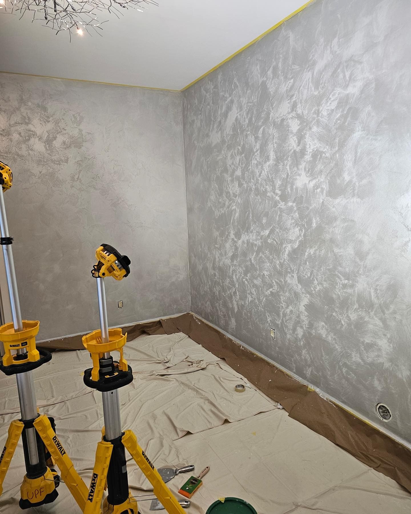 Silver textured walls in a room, illuminated by two yellow work lights.
