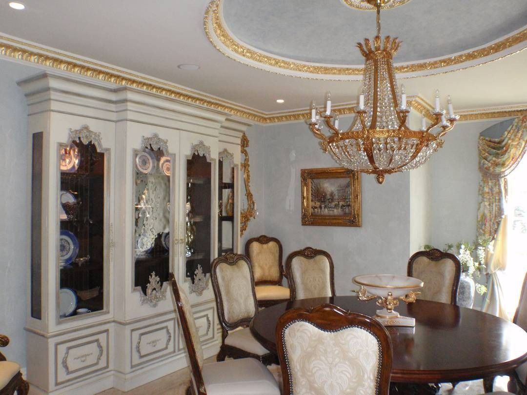 Elegant dining room: ornate white hutch, gold chandelier, oval table, and antique chairs. Blue walls, gold accents.