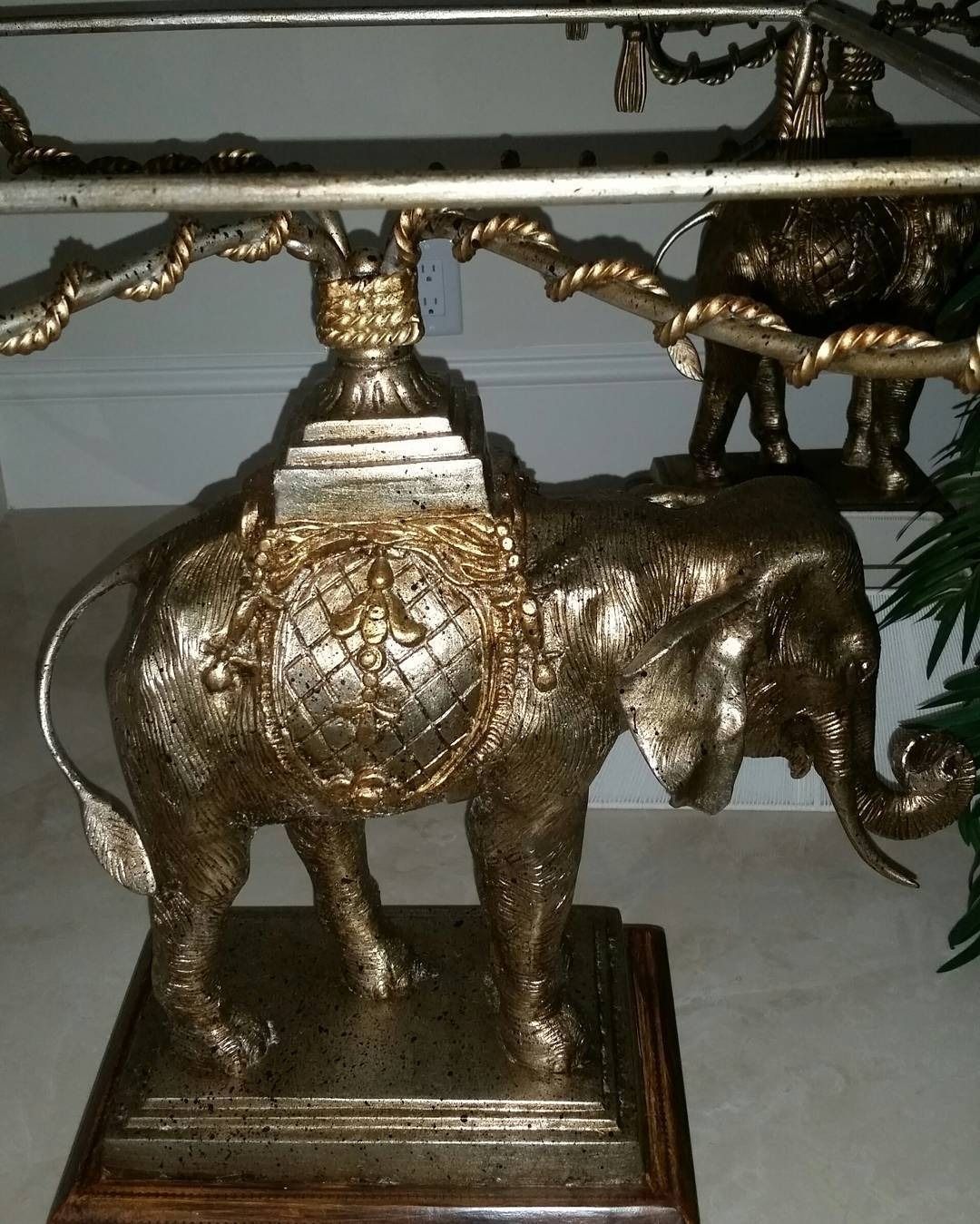 Gold elephant table base, ornate carvings, supporting a table surface, indoor setting.