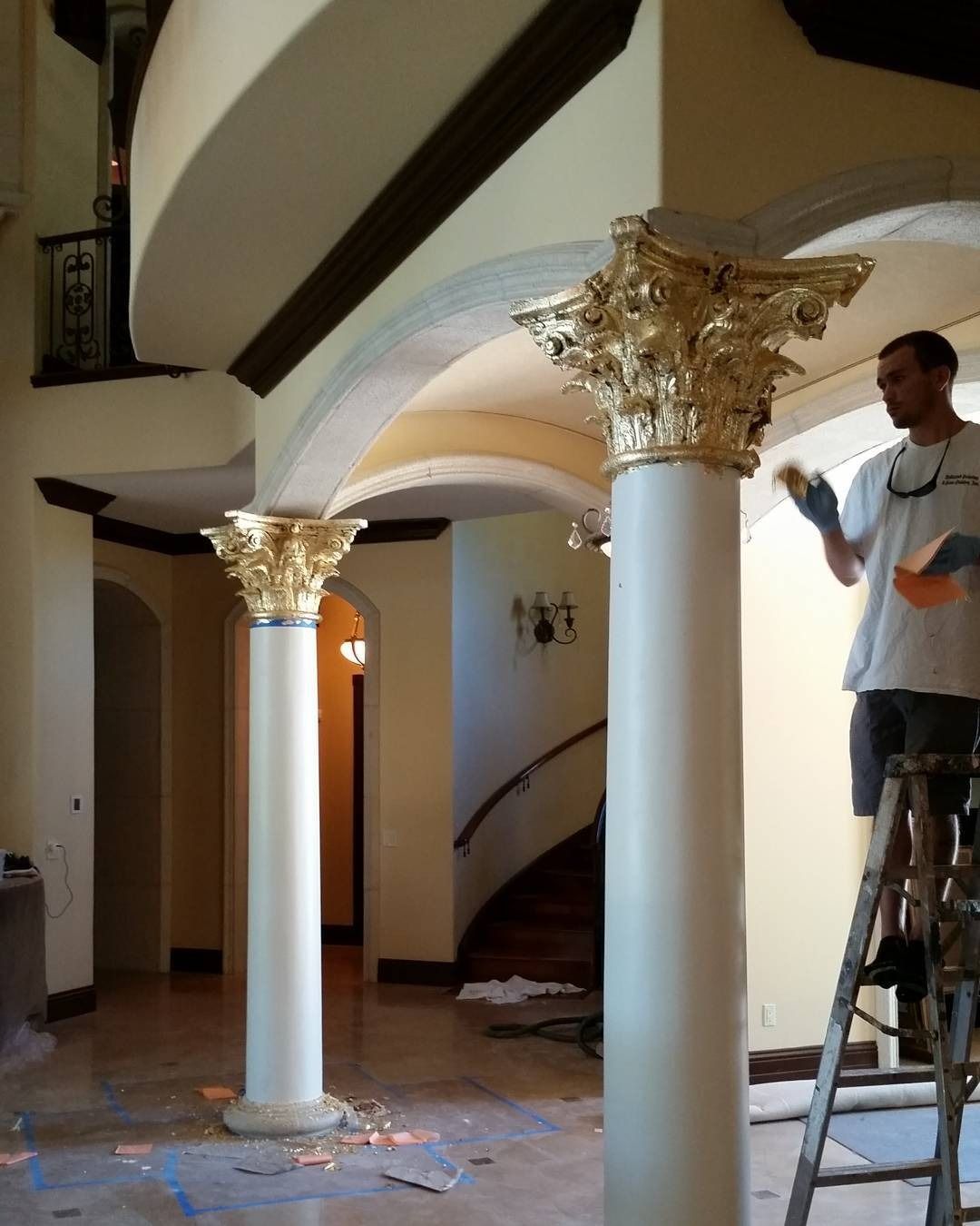 Man gilding the gold capital of a white column. Interior shot of a foyer with spiral staircase.