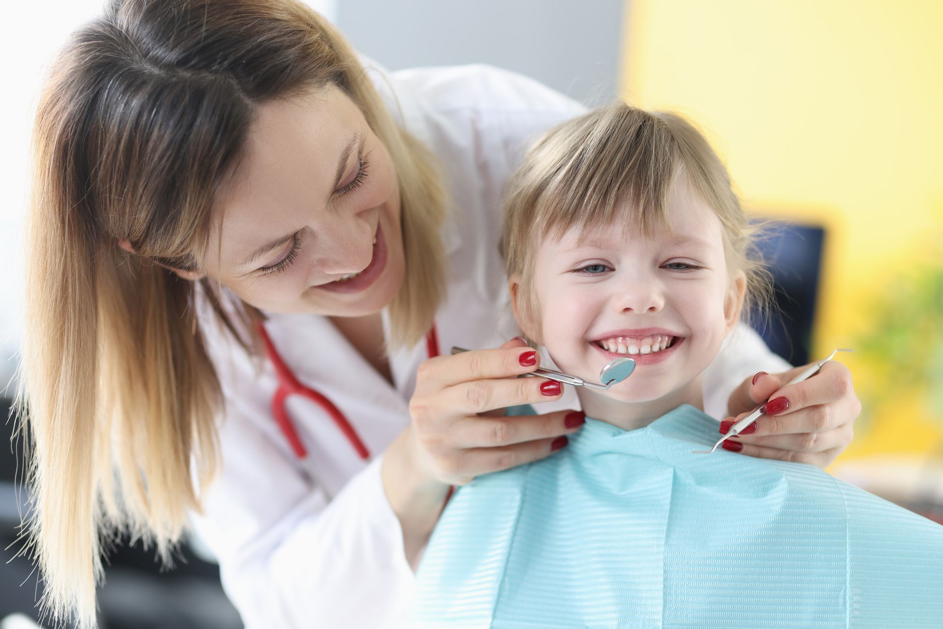 Dentist examining a child's teeth, both smiling. A dental chair and tools are visible.