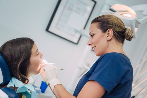 Dentist examining young girl's teeth during pediatric dental checkup in modern clinic.