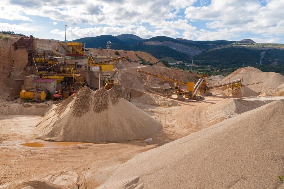 A large pile of sand in a quarry with mountains in the background.