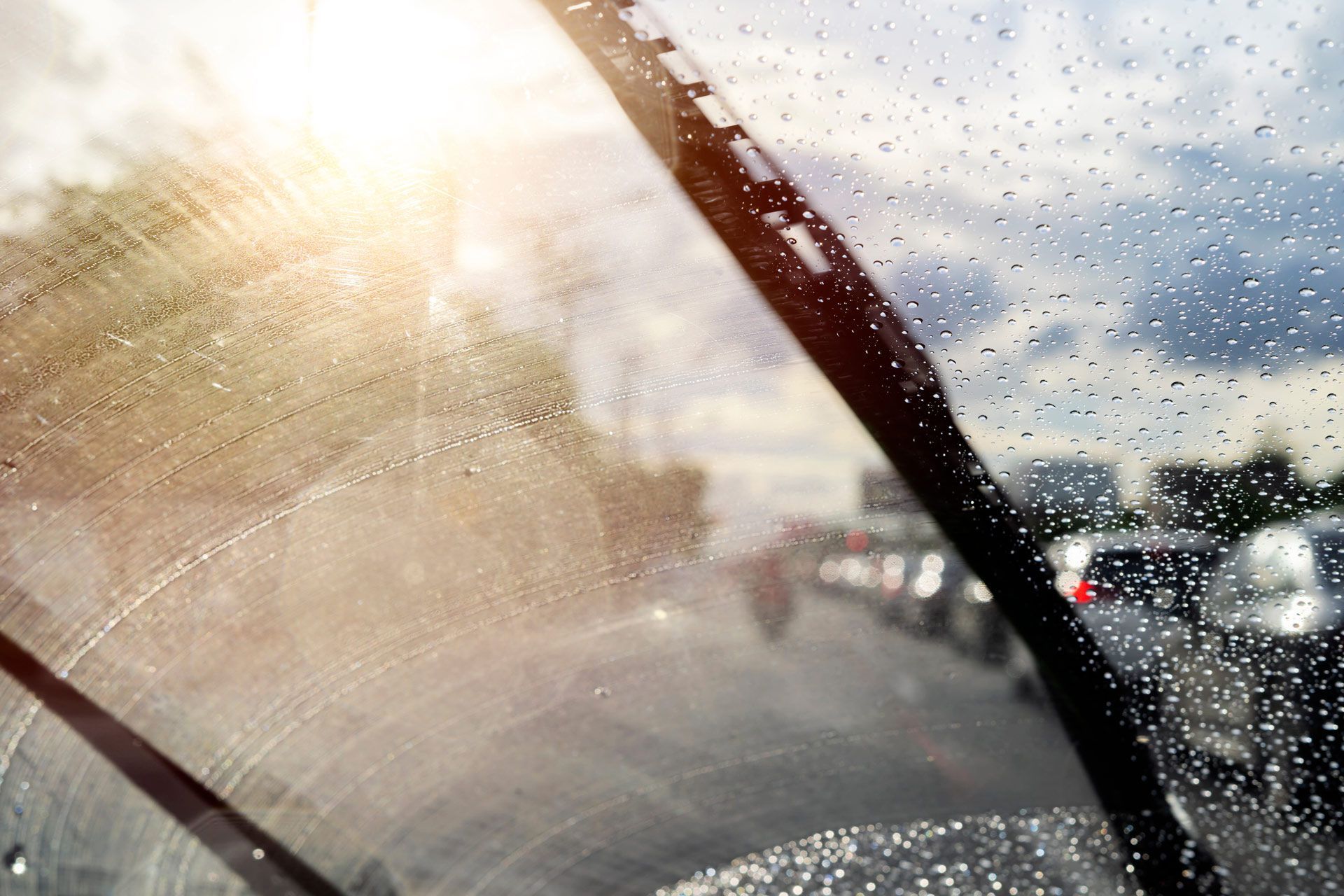 Rainy car windshield with sun glare and blurred traffic beyond the glass Rainy car windshield with sun glare and blurred traffic beyond the glass