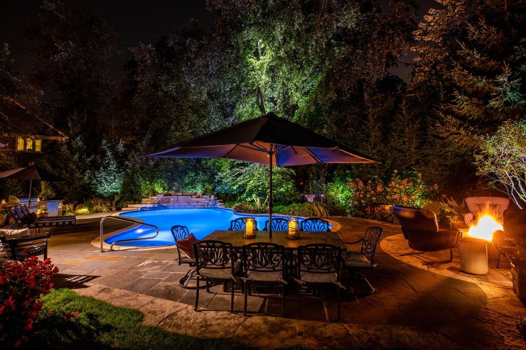 A patio area with a table , chairs , umbrella and fire pit at night.