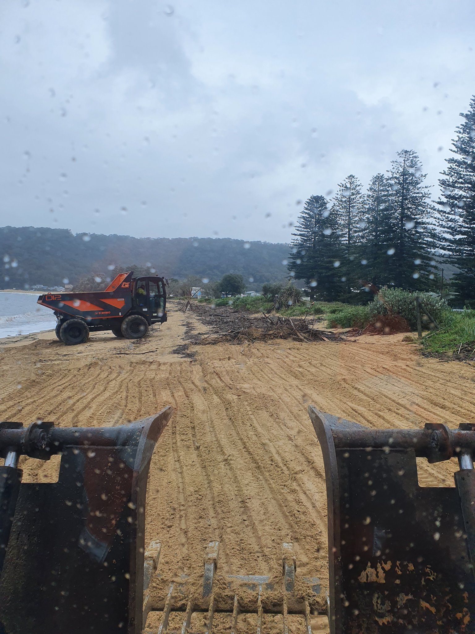 A dump truck is driving down a dirt road next to a beach. — Adam Lowe Earthmoving Pty Ltd in Somersby, NSW