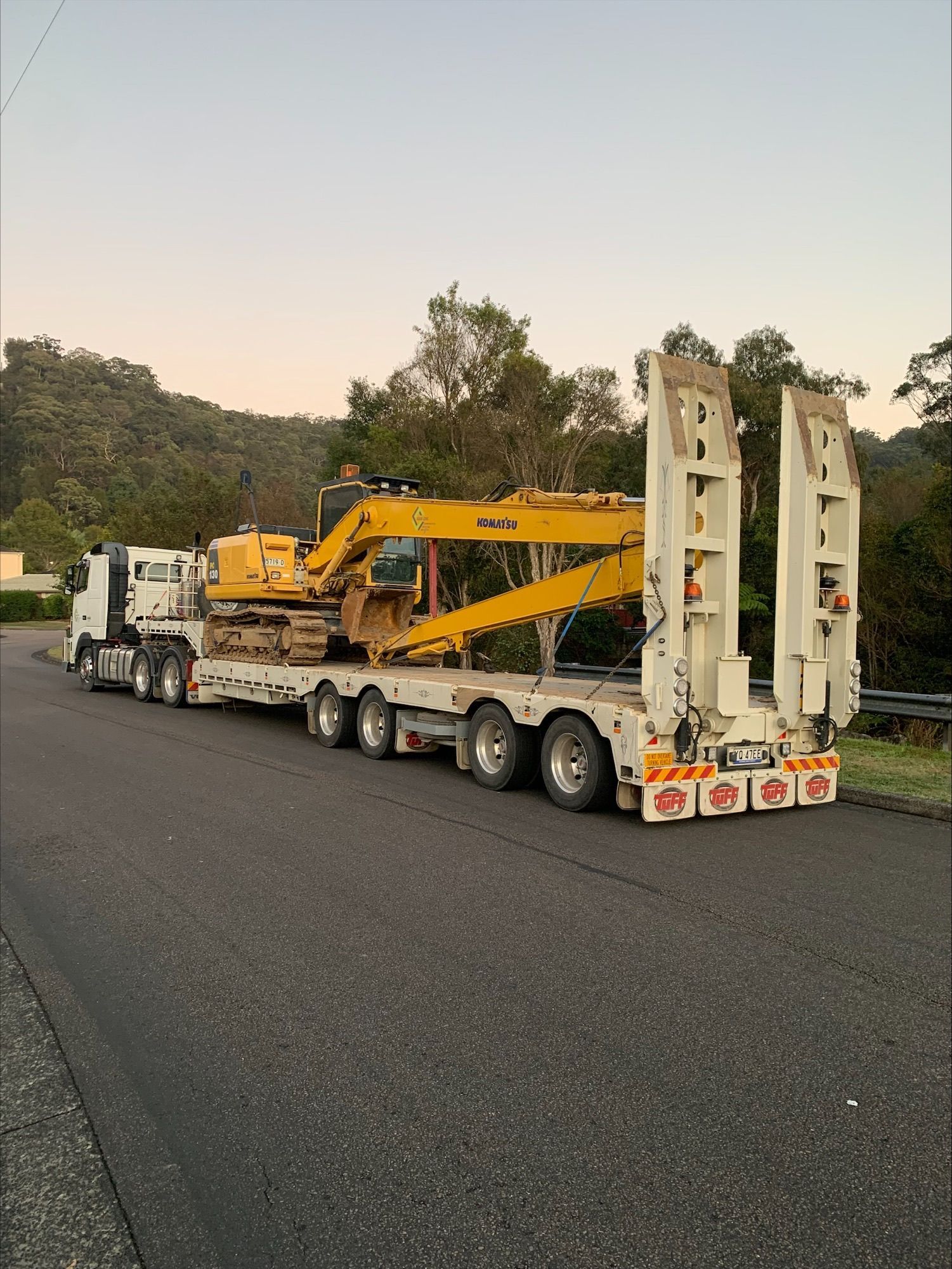 A truck is carrying a yellow excavator on a trailer. — Adam Lowe Earthmoving Pty Ltd in Somersby, NSW