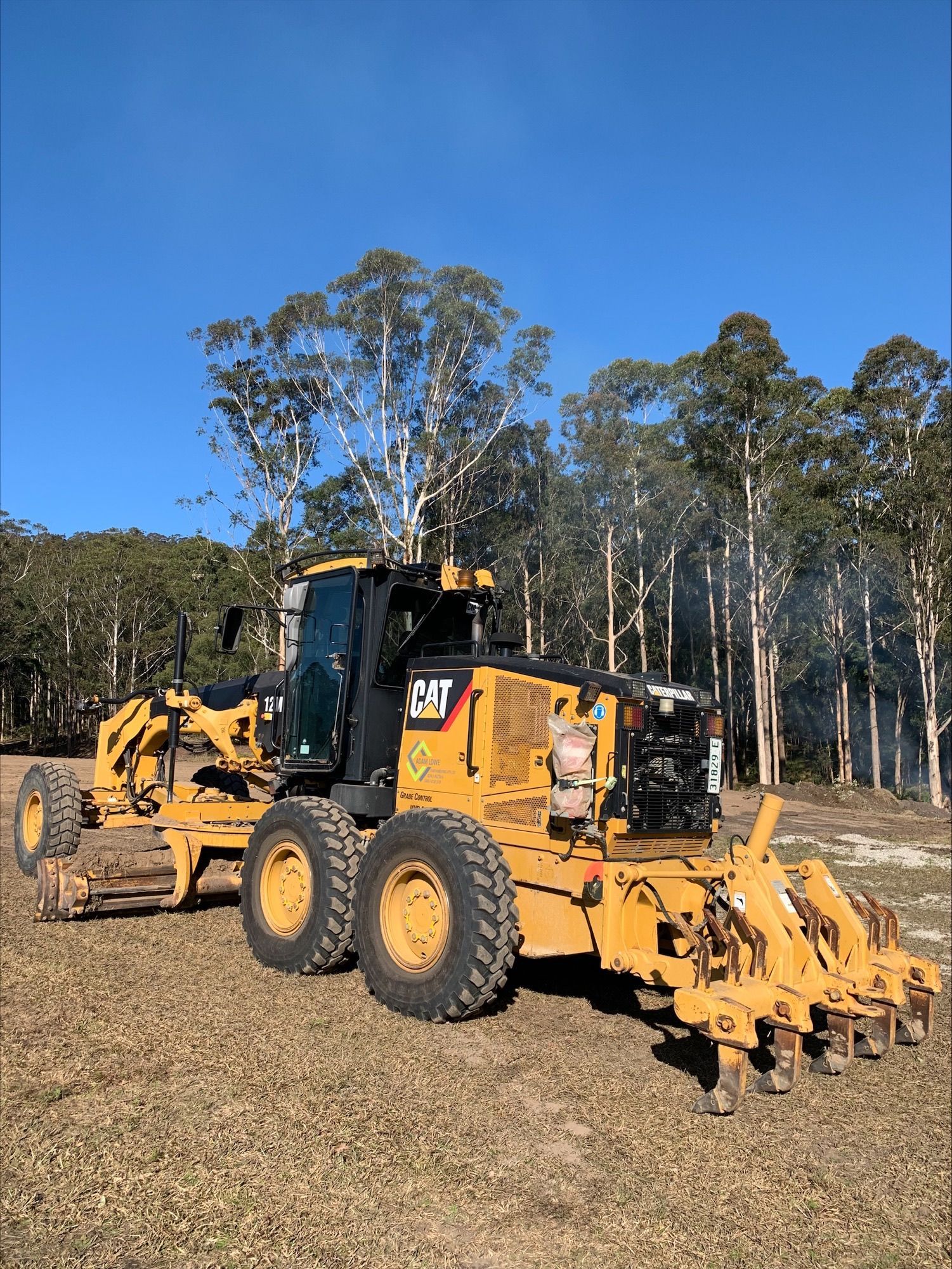 A yellow tractor is parked in a field with trees in the background. — Adam Lowe Earthmoving Pty Ltd in Somersby, NSW