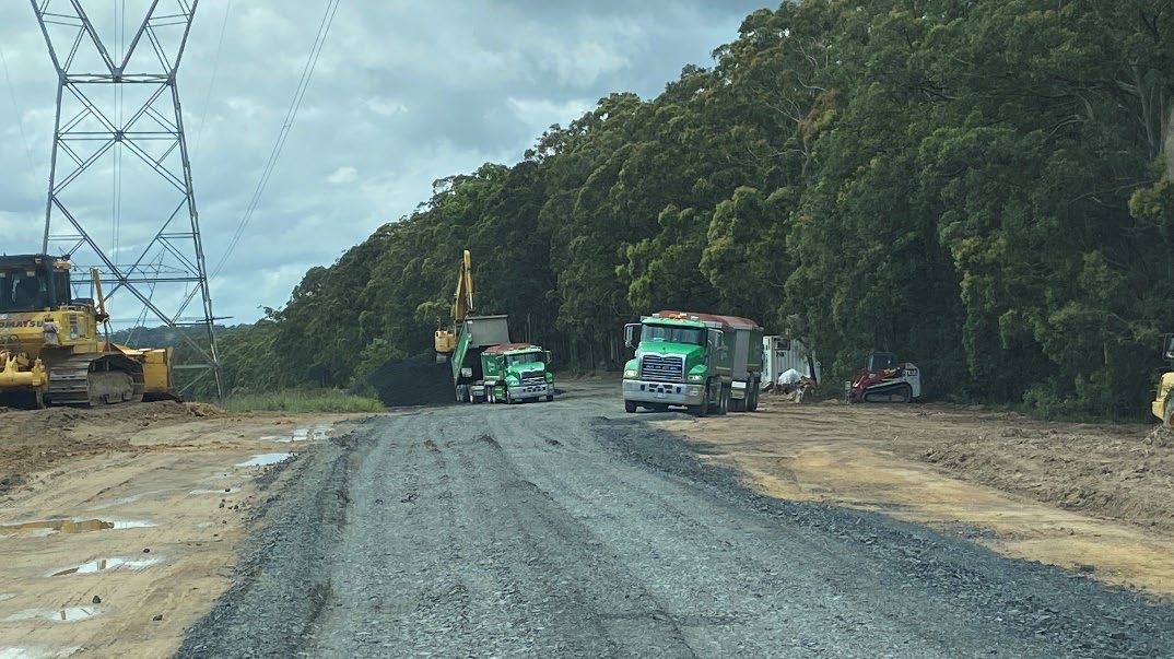 A couple of trucks are driving down a dirt road. — Adam Lowe Earthmoving Pty Ltd in Somersby, NSW