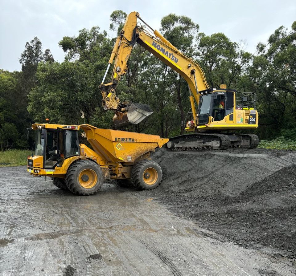 A yellow dump truck is being loaded with dirt by a yellow excavator. — Adam Lowe Earthmoving Pty Ltd in Somersby, NSW