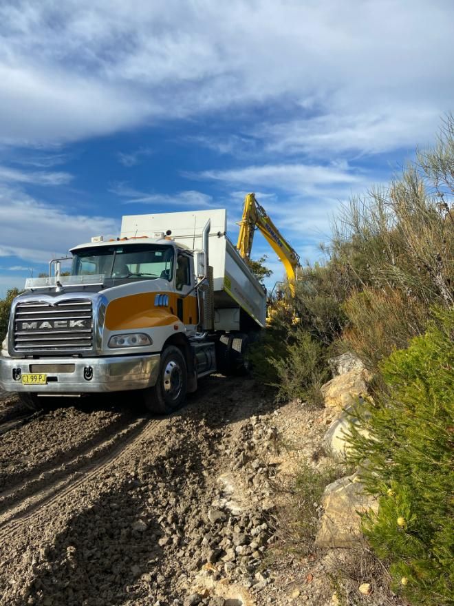 A Dump Truck Is Driving Down a Dirt Road — Adam Lowe Earthmoving Pty Ltd in Somersby, NSW