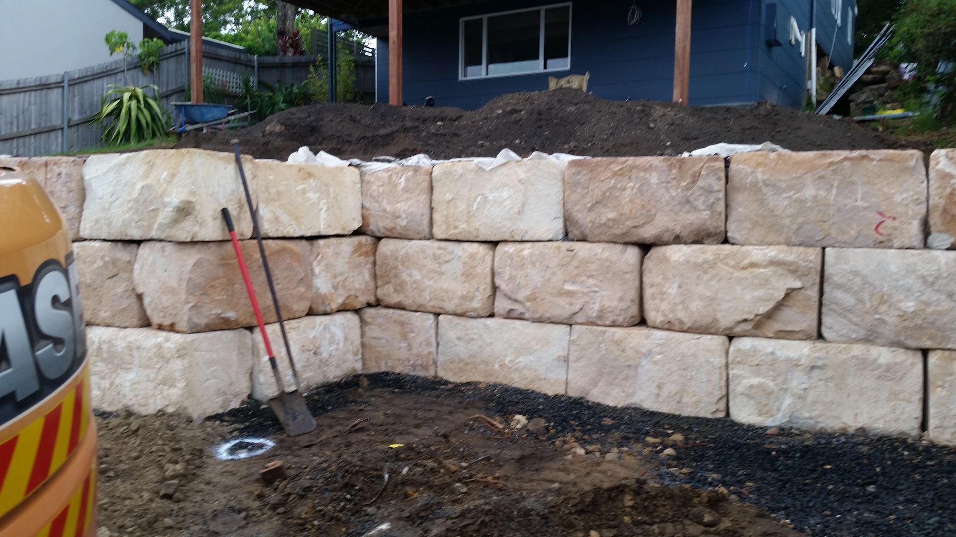 A large stone wall is being built in front of a house. — Adam Lowe Earthmoving Pty Ltd in Somersby, NSW