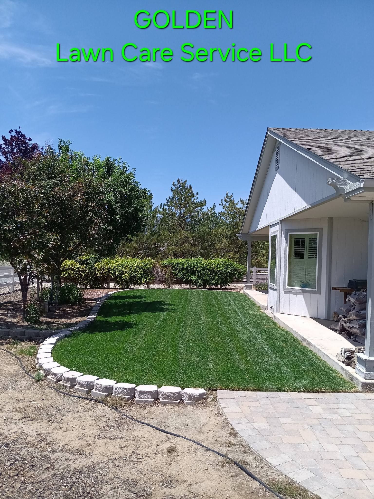 Landscaped front yard with green lawn, stone border, and house under a blue sky, labeled Golden Lawn Care Service LLC
