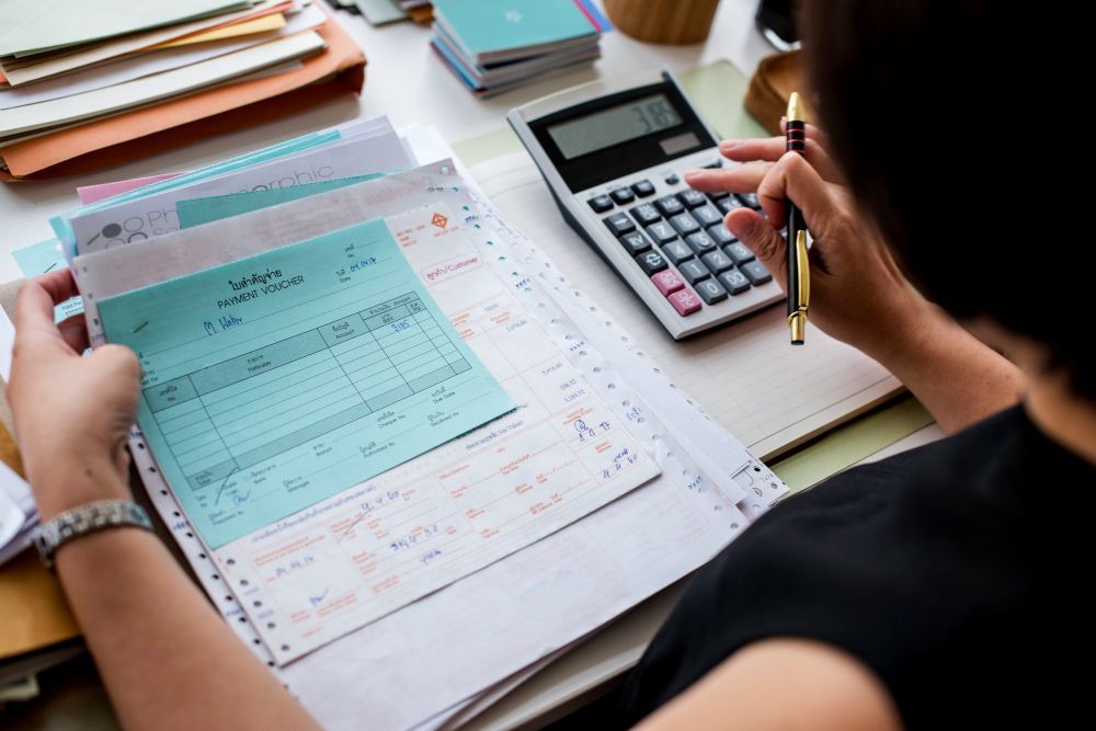 A woman is sitting at a desk using a calculator and a pen.