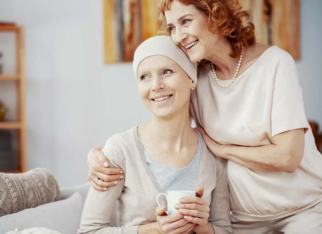 Two women are sitting next to each other on a couch . one of the women is holding a cup of coffee.
