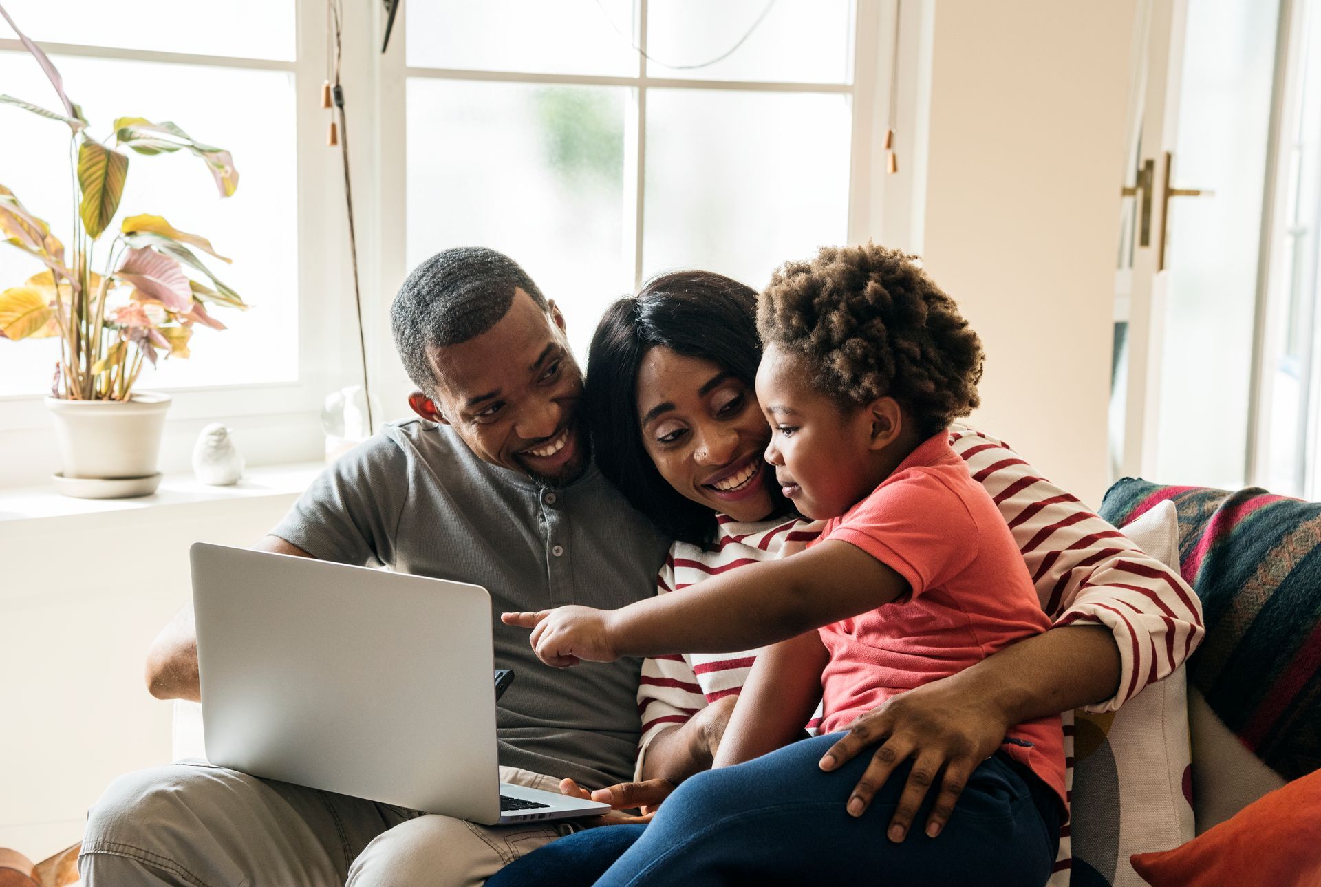 A family is sitting on a couch looking at a laptop computer.