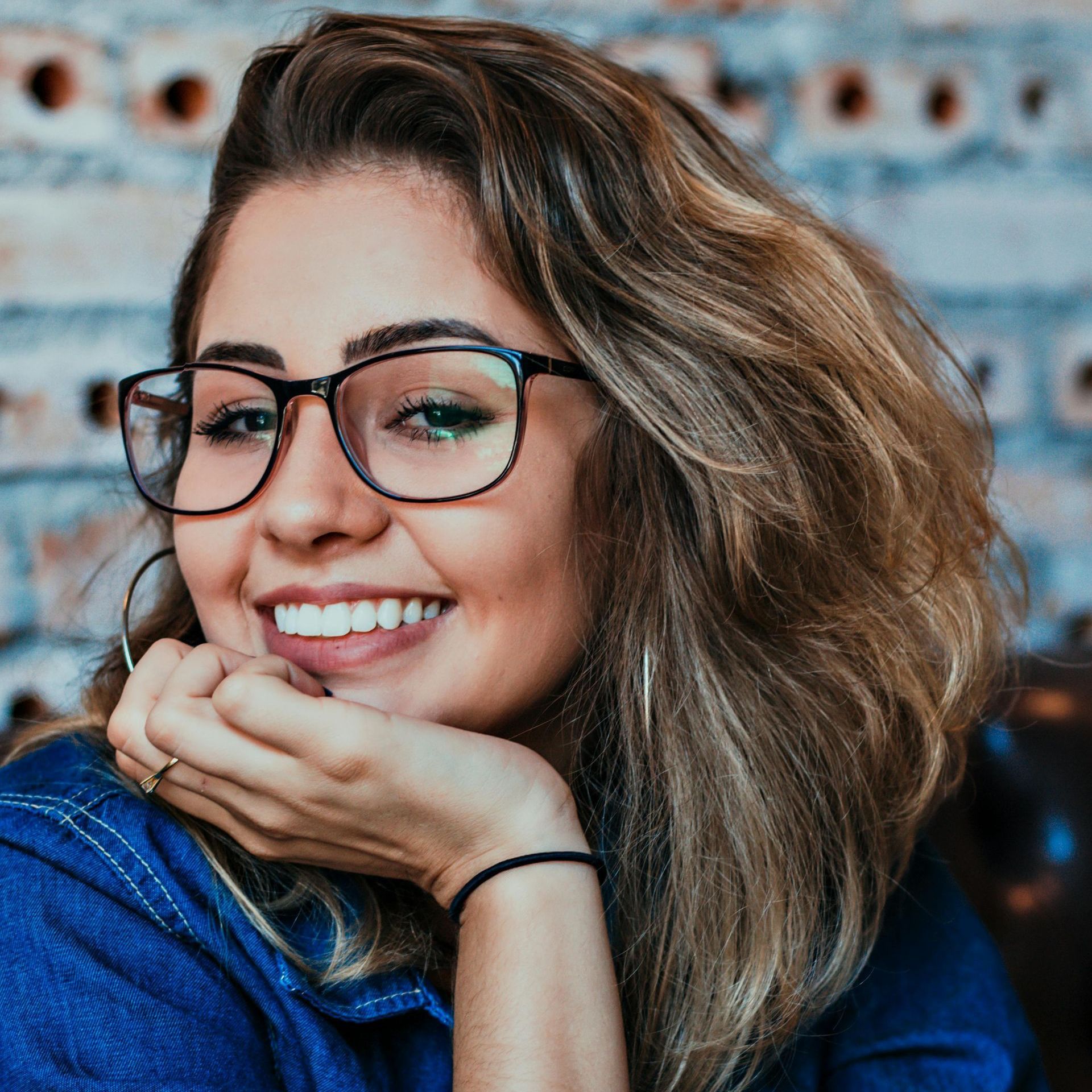 A woman wearing glasses is smiling with her hand on her chin.
