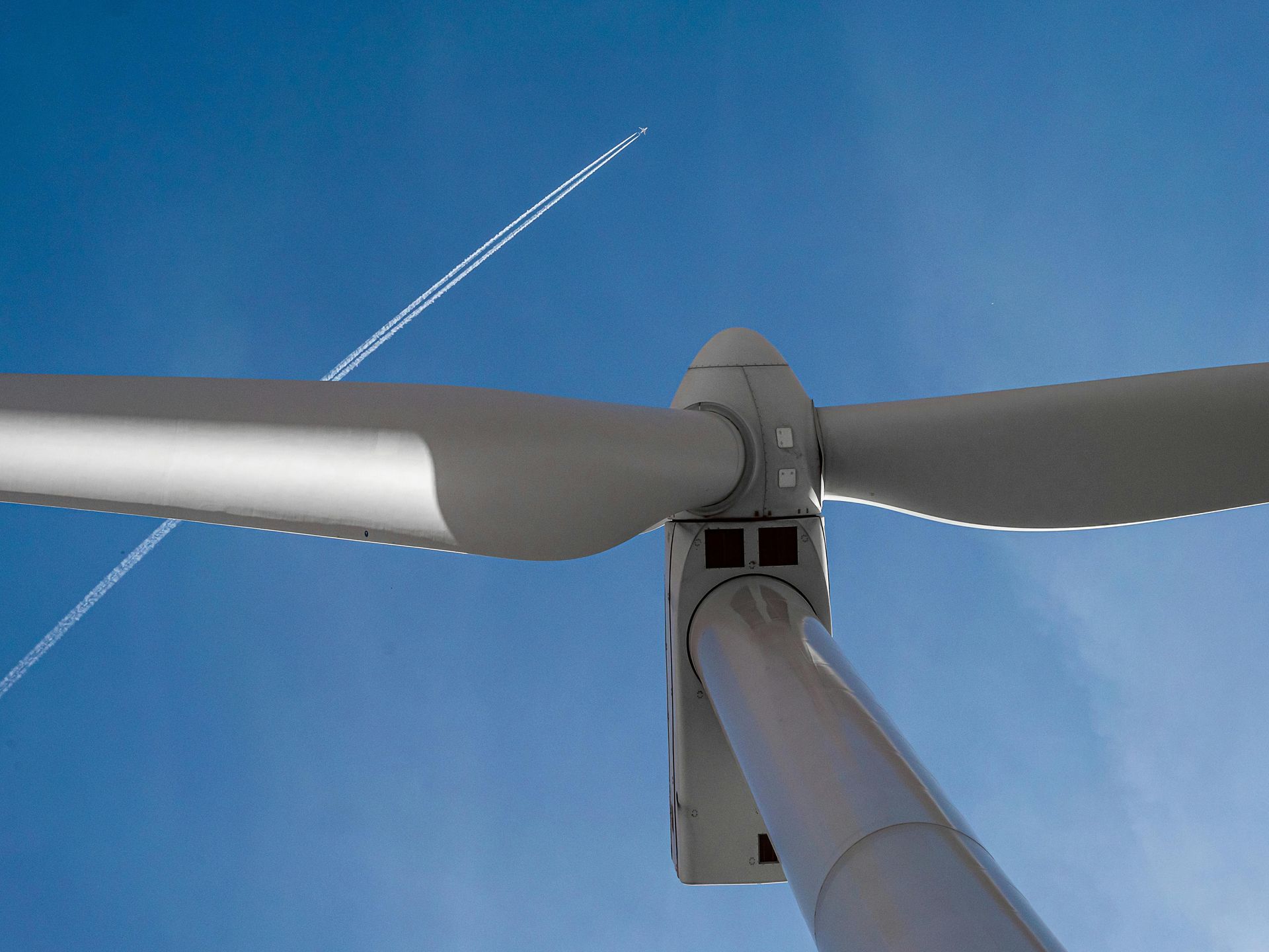 Wind turbine against a blue sky, with contrails from a plane.