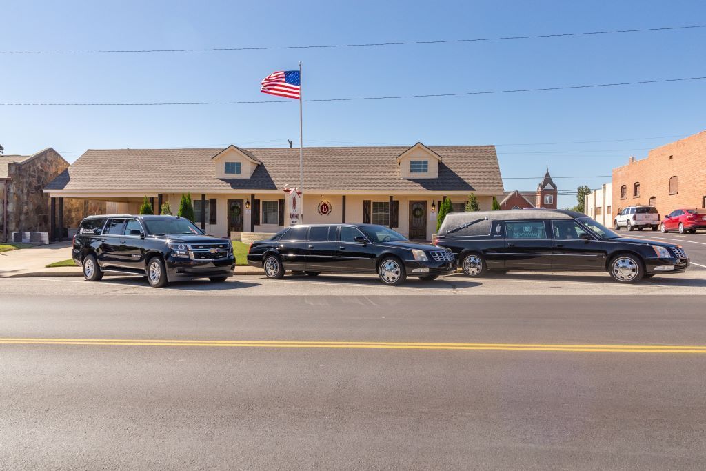 Three black limousines are parked on the side of the road in front of a building.