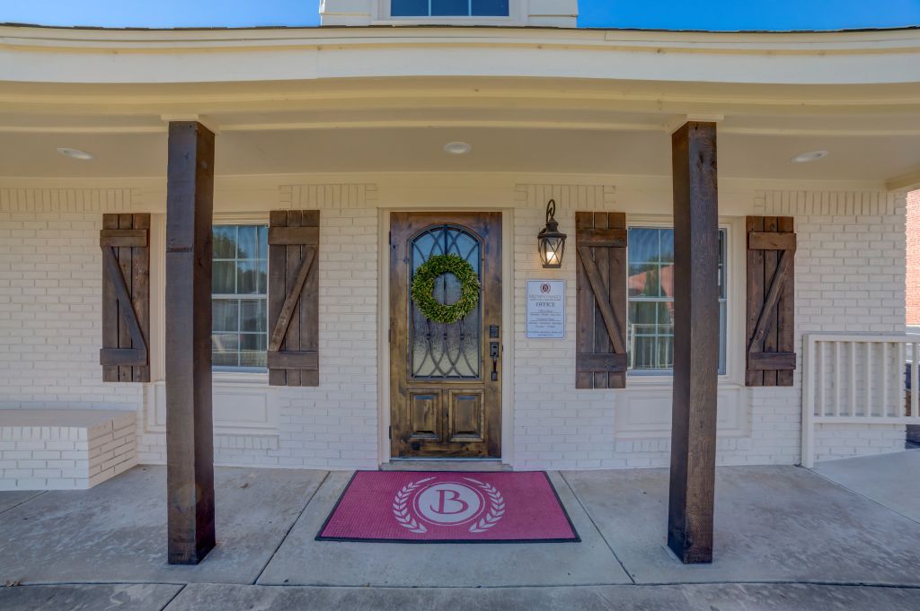 The front of a house with a door and a red mat with the letter b on it