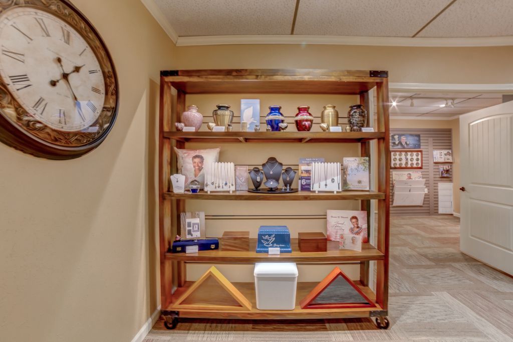 A clock is hanging above a wooden shelf with a lot of items on it.