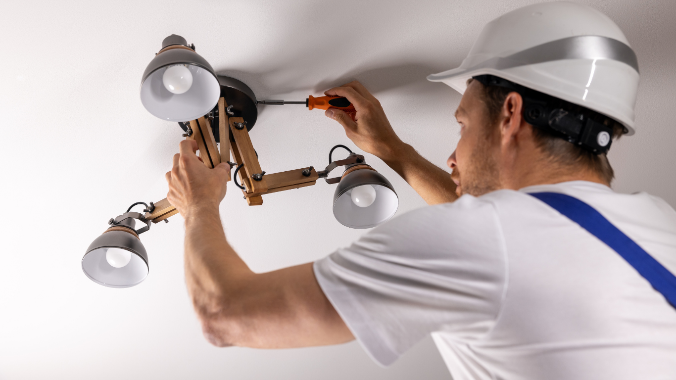 Electrician installing a ceiling light fixture with tools on a white ceiling
