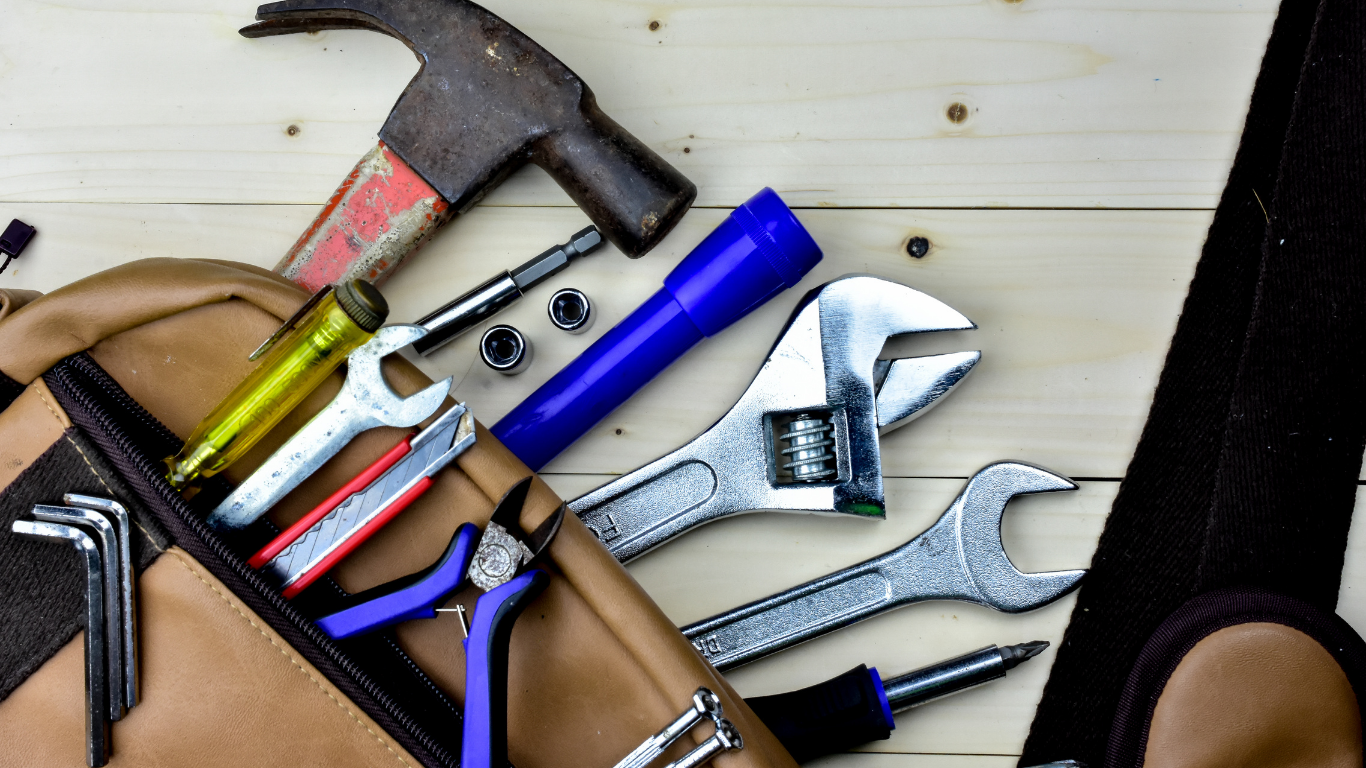 Assorted hand tools in a tool bag, including a hammer, wrenches, and screwdriver on a workbench.
