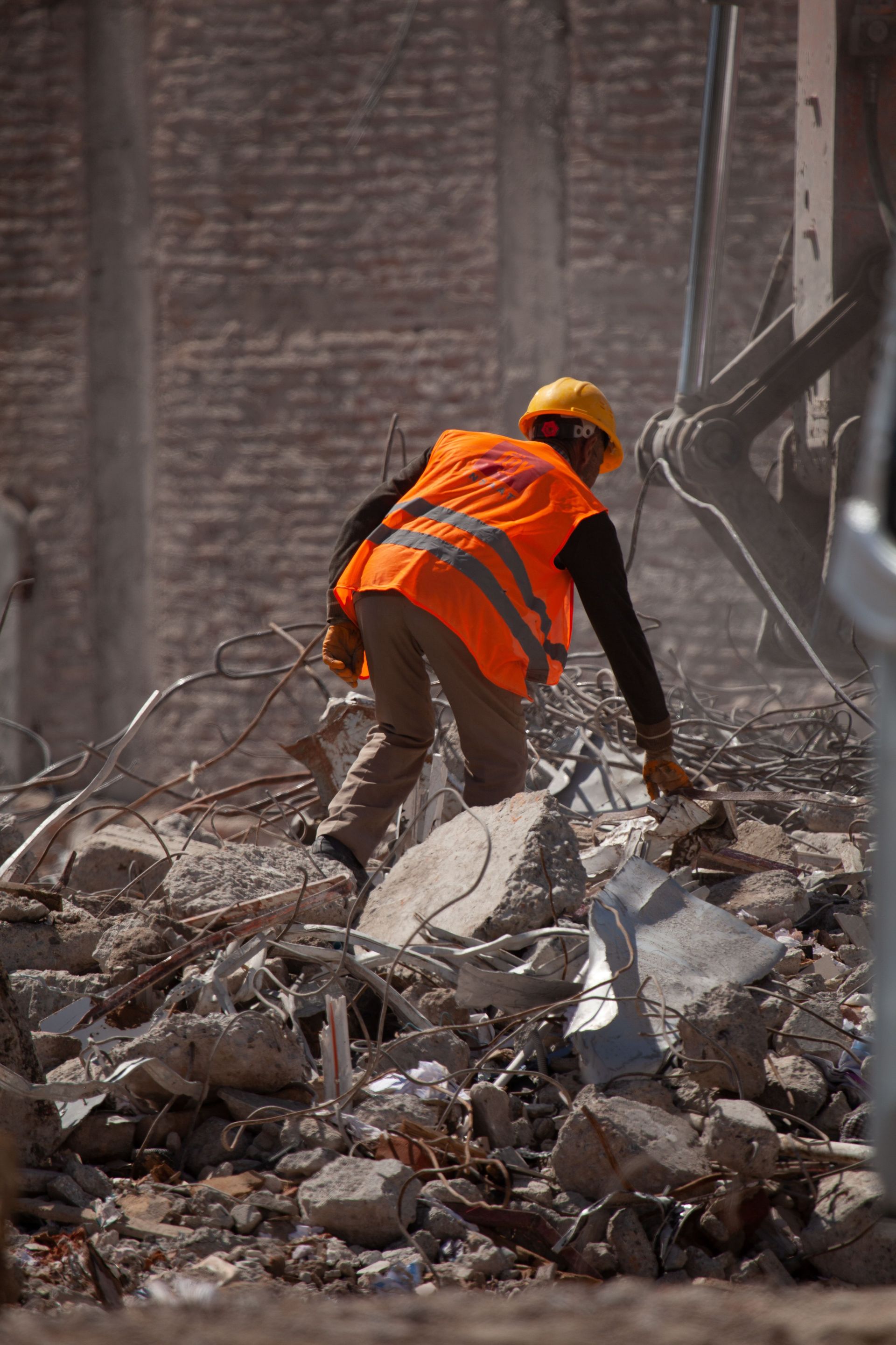 Worker in orange safety vest and yellow hard hat clearing rubble at a demolition site