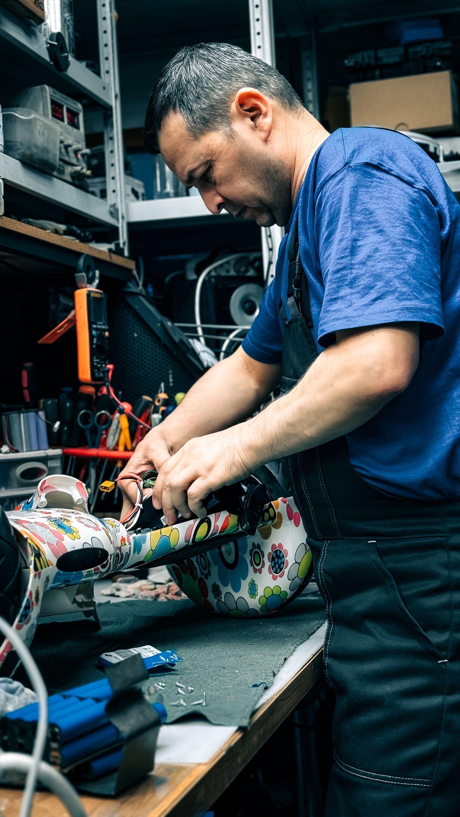 Technician working on a colorful guitar in a cluttered workshop surrounded by tools and equipment