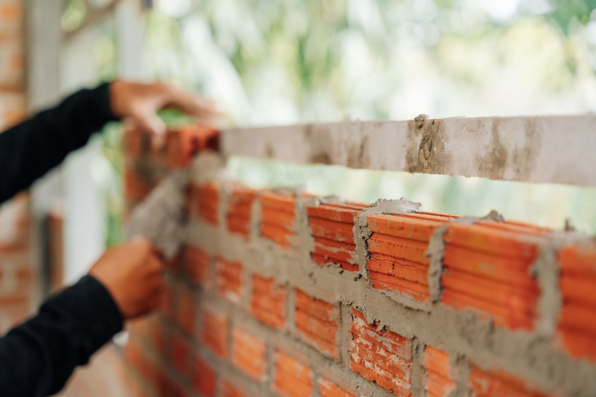 Person building a brick wall with cement, trowel, and level tool. Person building a brick wall with cement, trowel, and level tool.