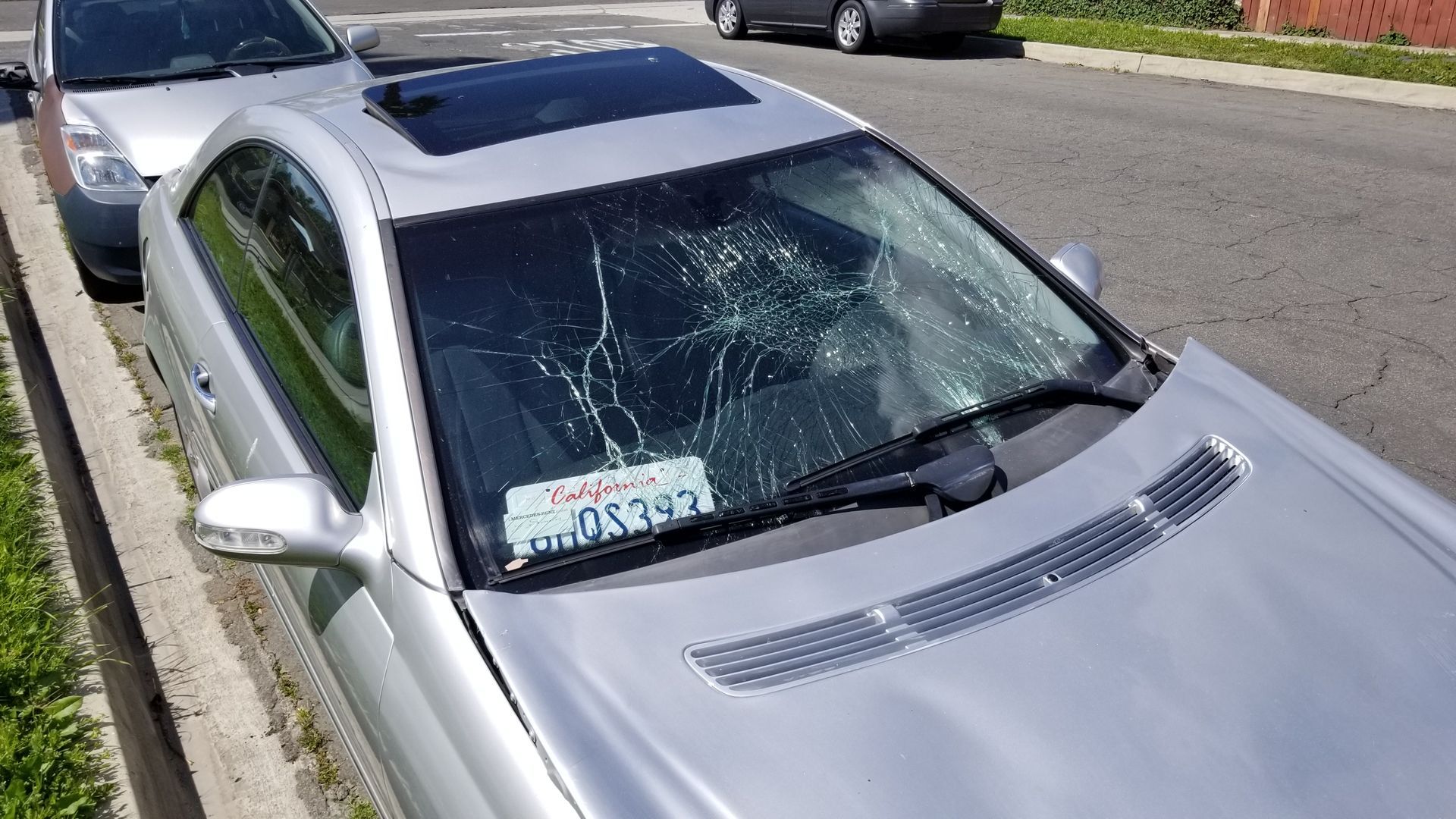 A silver car with a broken windshield is parked on the side of the road.