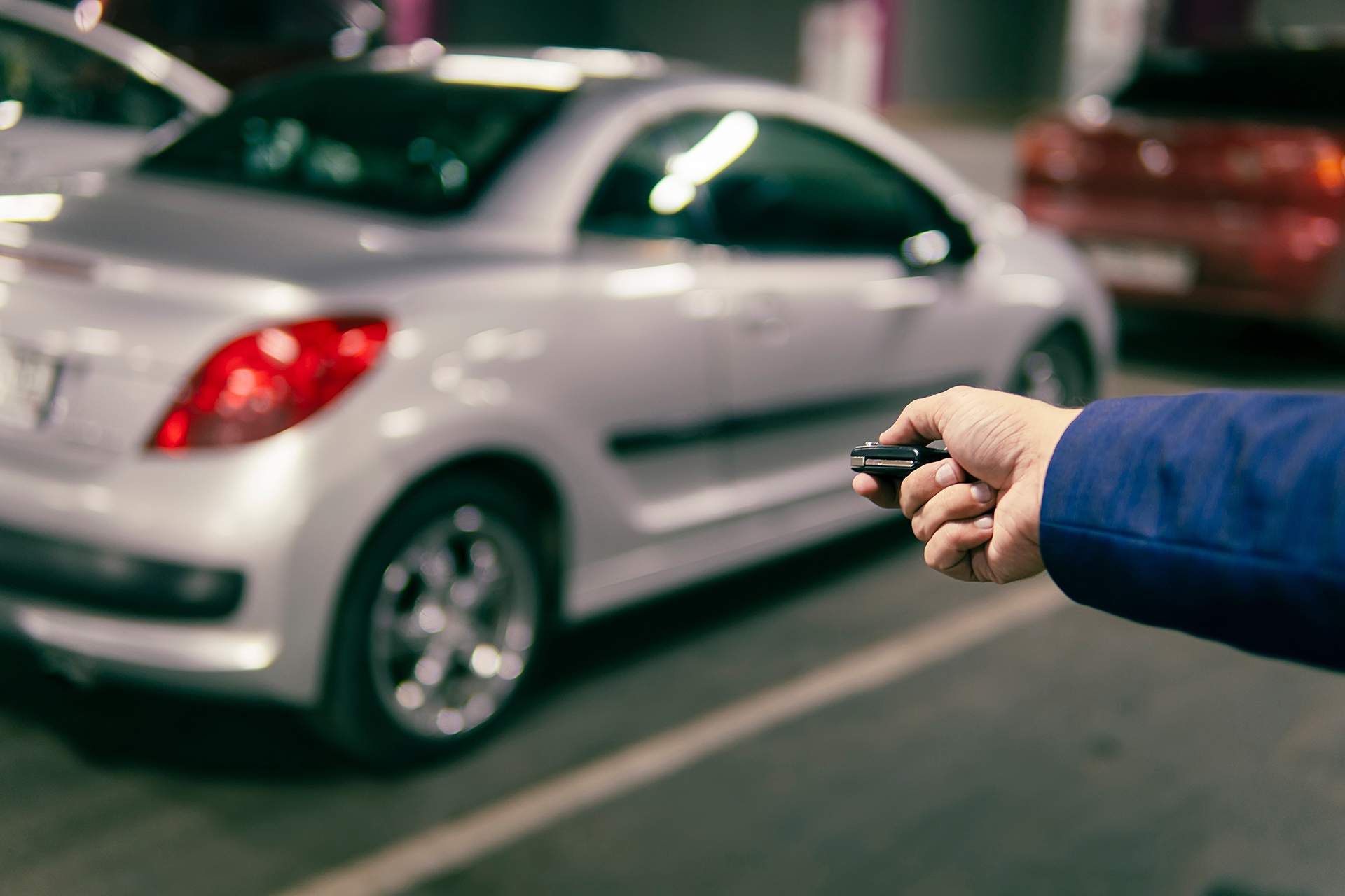 A person is holding a remote control in front of a car.
