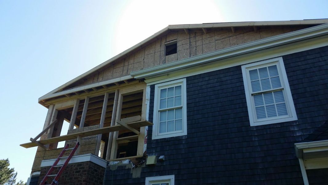House under construction, framing visible. New siding in progress, with blue and white trim. Bright sunny day.
