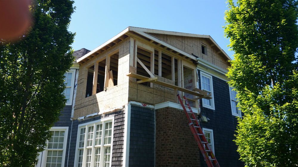 Construction of an addition on a dark blue building, with a wood frame and scaffolding, under a blue sky.