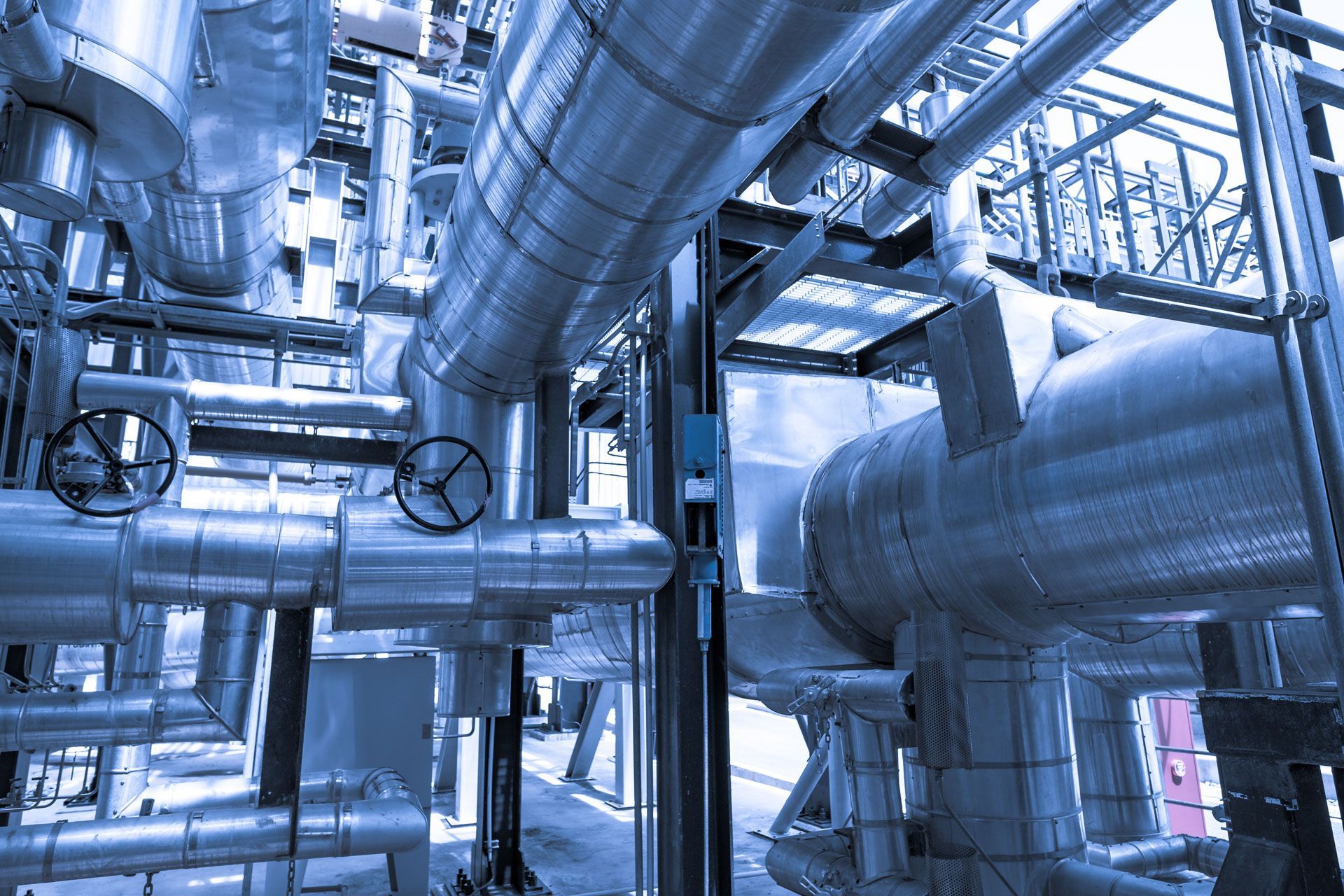 Complex industrial piping system, wrapped in insulation, with valves. Blue-toned lighting.